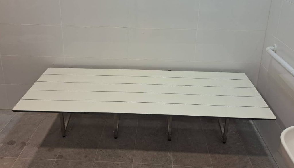 מיטת הלבשה מתקפלת נגישה לנכים, עמידה למים, רגליים מנירוסטה, עבור מקלחות נגישות, מלתחות נכים או תא משולב נגיש.